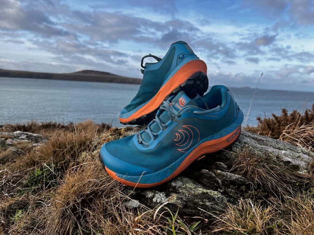 Picture of the Topo MTN Racer 3 in blue and orange on a mossy rock